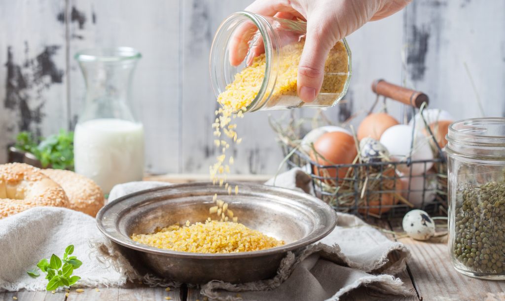 Raw bulgur heap in a metal bowl | Meglepetés száraz bulgurt önt a tálba egy nő