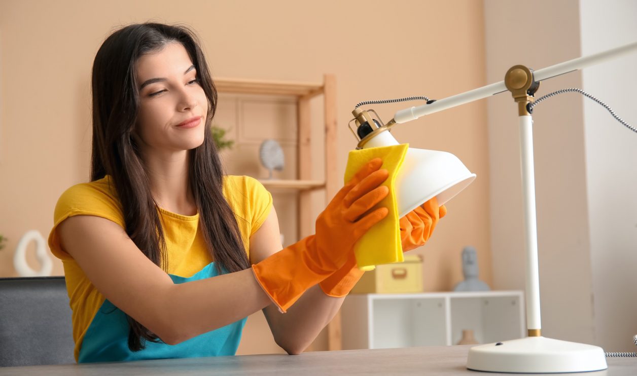 Young woman cleaning lamp with rag in living room | Meglepetés