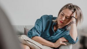 gondterhelt klimaxoló nő ül a kanapén szomorúan mert hullik a haja