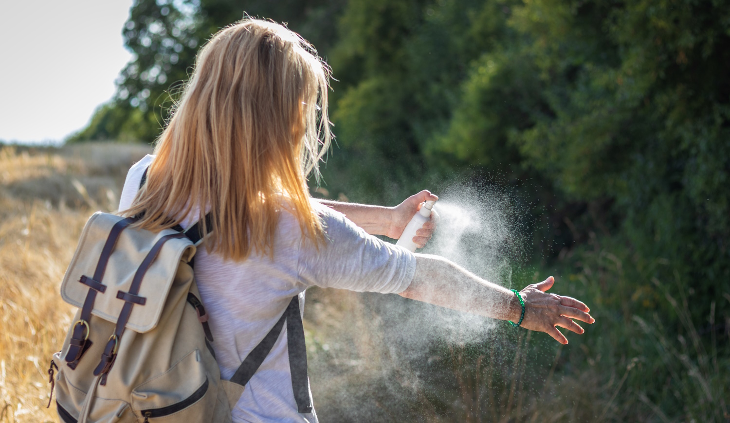 kullancsriasztó spray-t fúj magára a szőke nő az erdőben