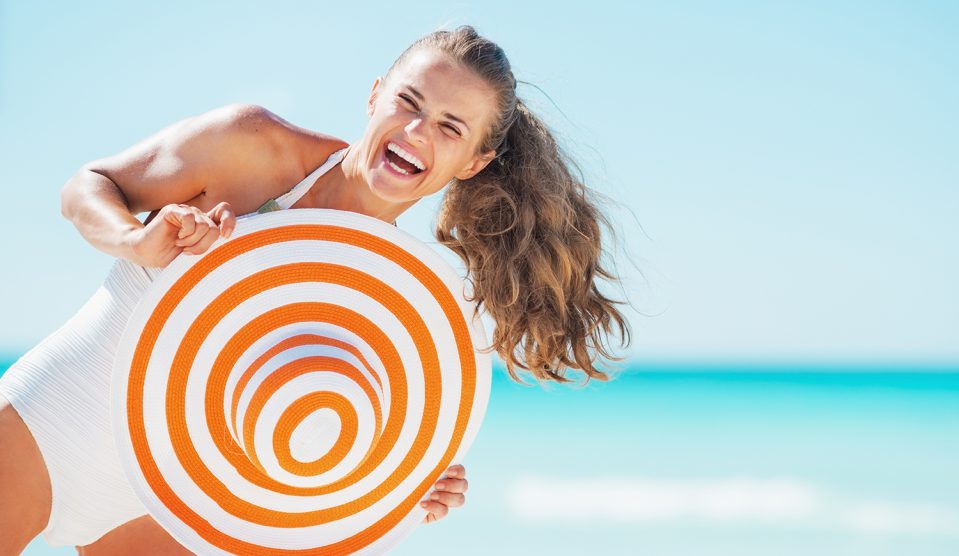 Boldog fiatal nő fürdőruhában, strandkalapban