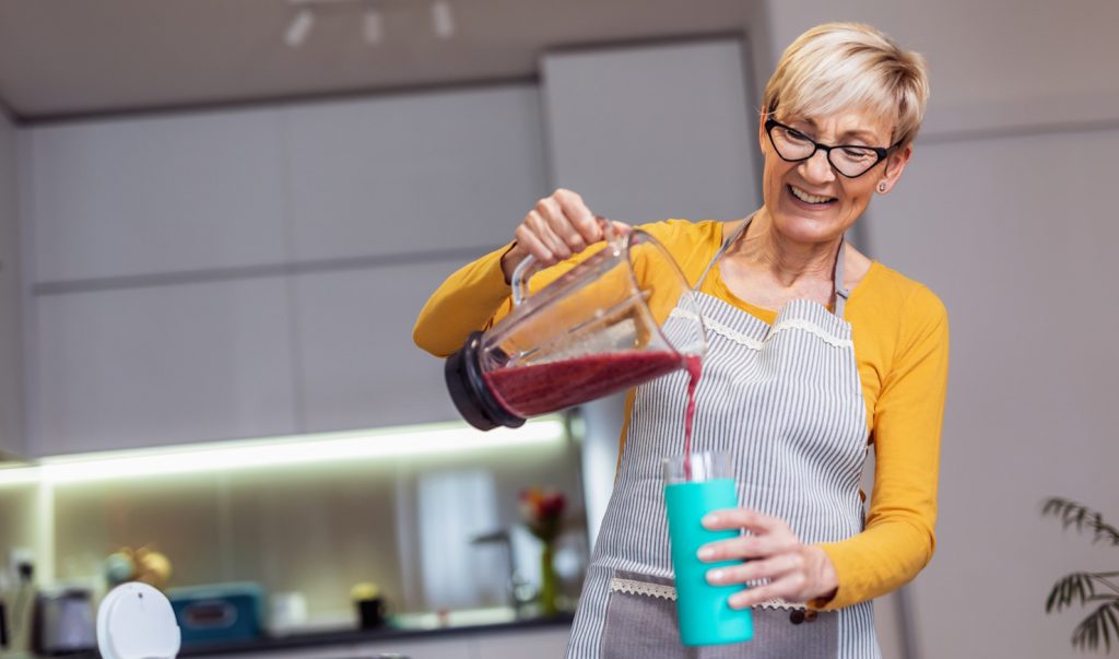 áfonya turmixot készít a konyhában egy idős hölgy