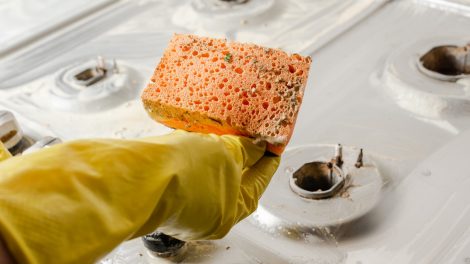 koszos gáztűzhelyet takarít sárga gumikesztyűben egy nő