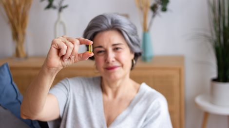 idős nő vitaminos kapszulát mutat a kamerába