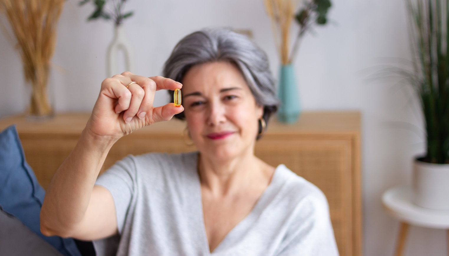 idős nő vitaminos kapszulát mutat a kamerába