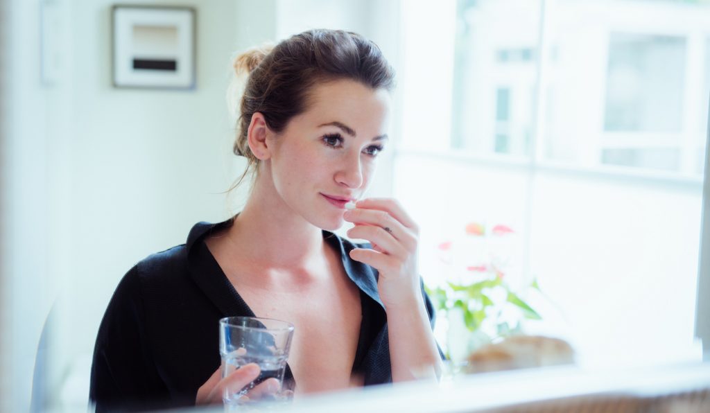 vitamint vesz be egy nőő a fürdőszobában a tükör előtt