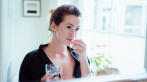vitamint vesz be egy nőő a fürdőszobában a tükör előtt