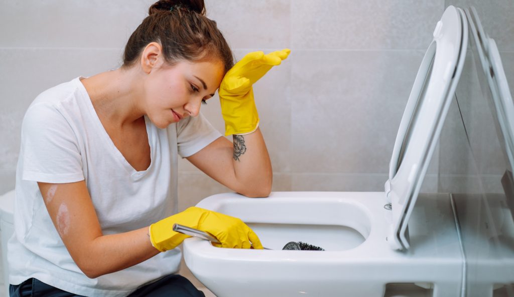 sárga gumikesztyűben wc-t takarít egy fiatal lány