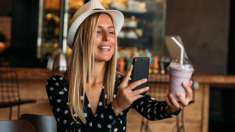 Fiatal nő kalapban smoothie-ját fotózza