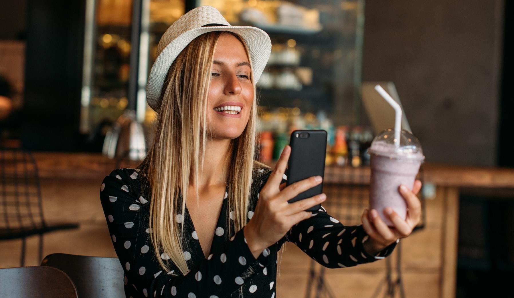 Fiatal nő kalapban smoothie-ját fotózza