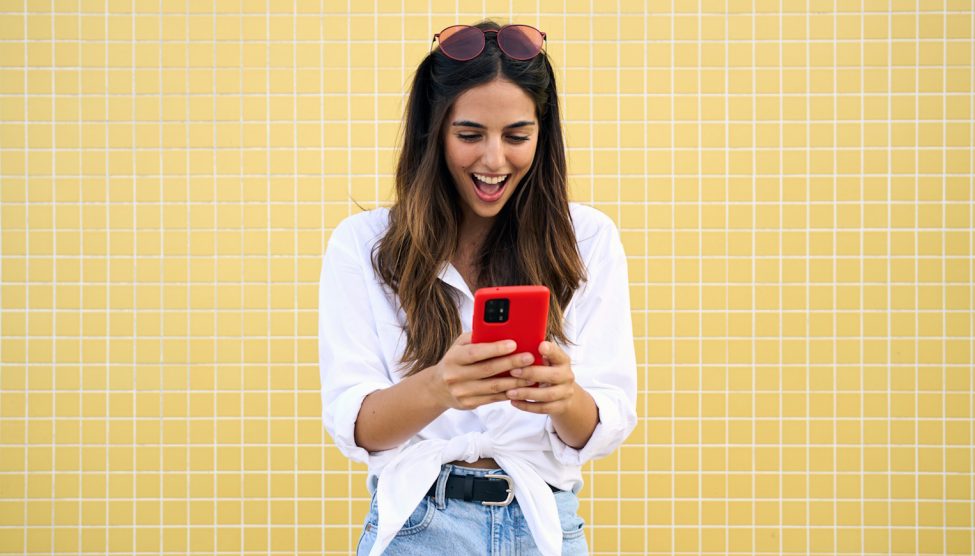 fiatal nő örül piros mobiltelefonnal a kezében