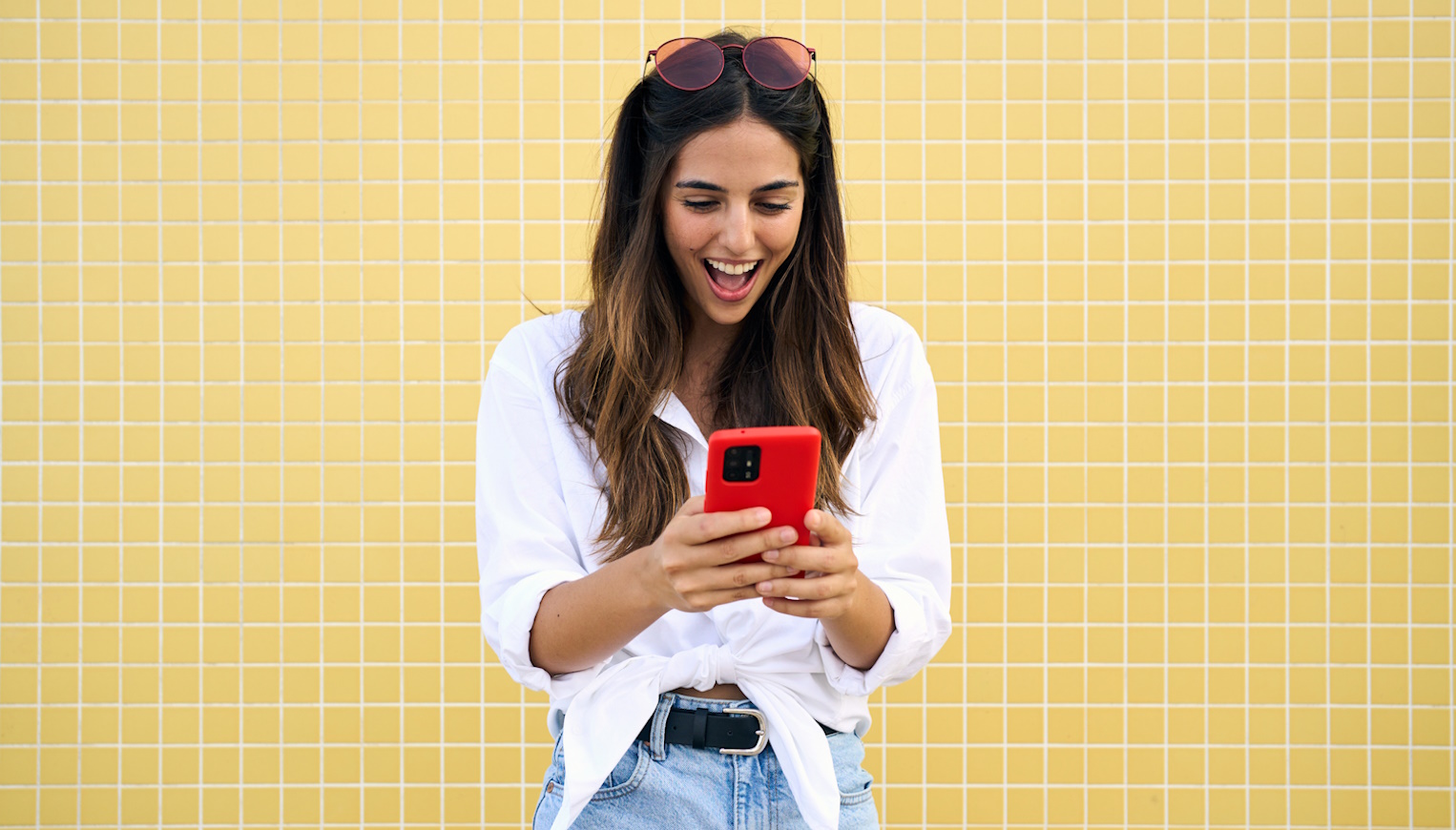fiatal nő örül piros mobiltelefonnal a kezében