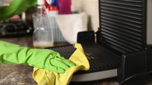 zöld gumikesztyűben grillt takarít a nő