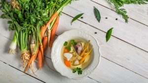 aranyló húsleves fehér tányérban mellette zöldségek