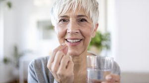 boldog idős nő d-vitamint vesz be egy pohár vízzel
