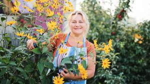 ősszel a virágoskertben mosolyog egy szőke nő