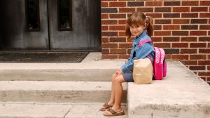 kislány iskolatáskával ül az iskola előtt