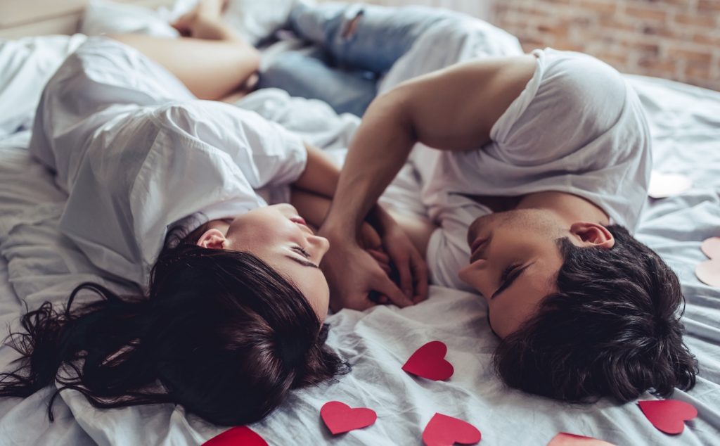 Egy pár fekszik az ágyben, fejük felett szivecskék