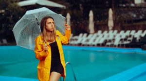 nő fürdőruhában kabátban esernyővel a medence szélén