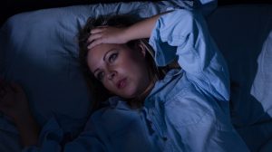nő nem tud aludni éjszaka fekszik az ágyban és fogja a fejét
