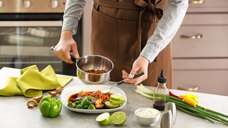 nő sárgarépát szószban tesz tányérra a konyhában