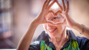 Idős nő mosolyogva fromáz szívet a kezével