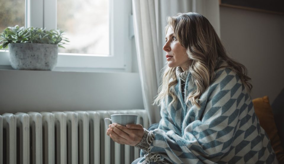 fűtés spórolás középkorú nő pokrócban ül a radiátor mellett