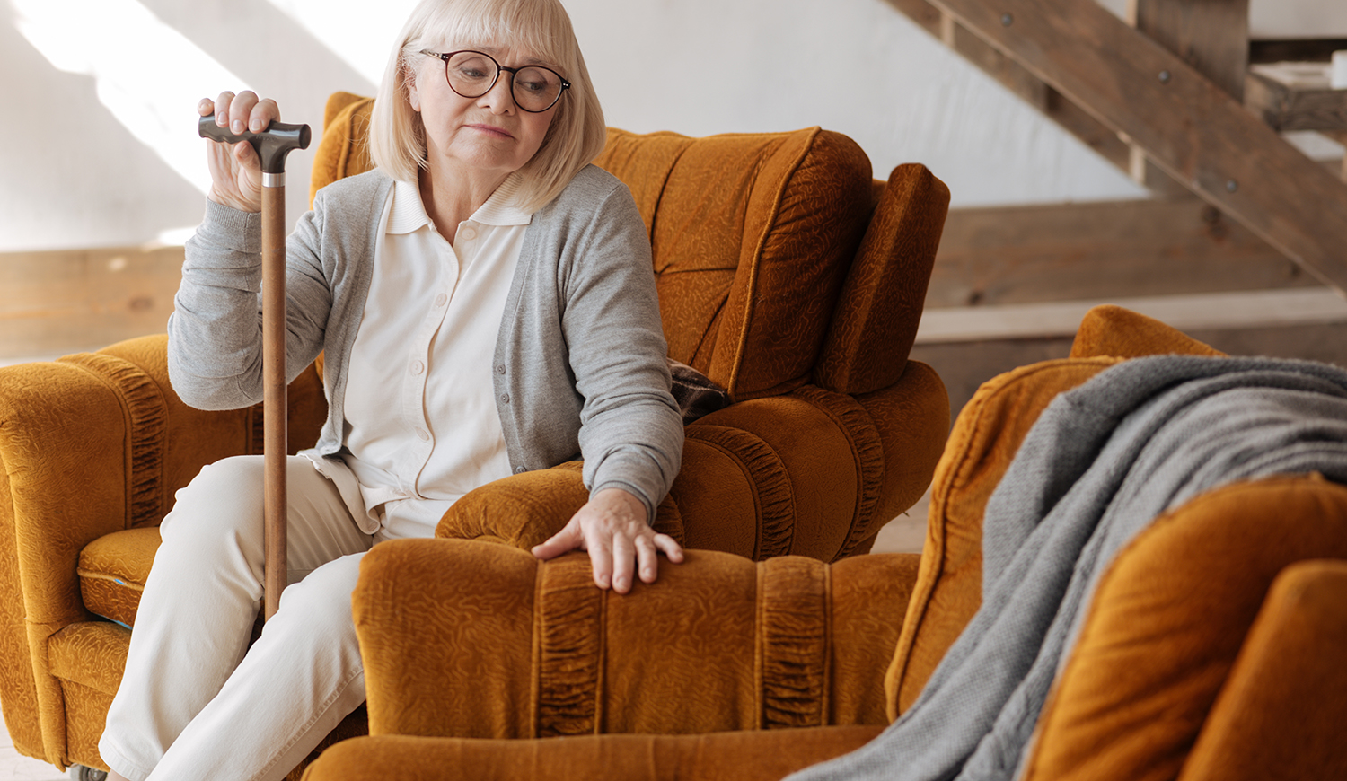 idős nő, sétapálcával a kezében, és a mellette lévő üres helyre néz, miközben a férjét gyászolja