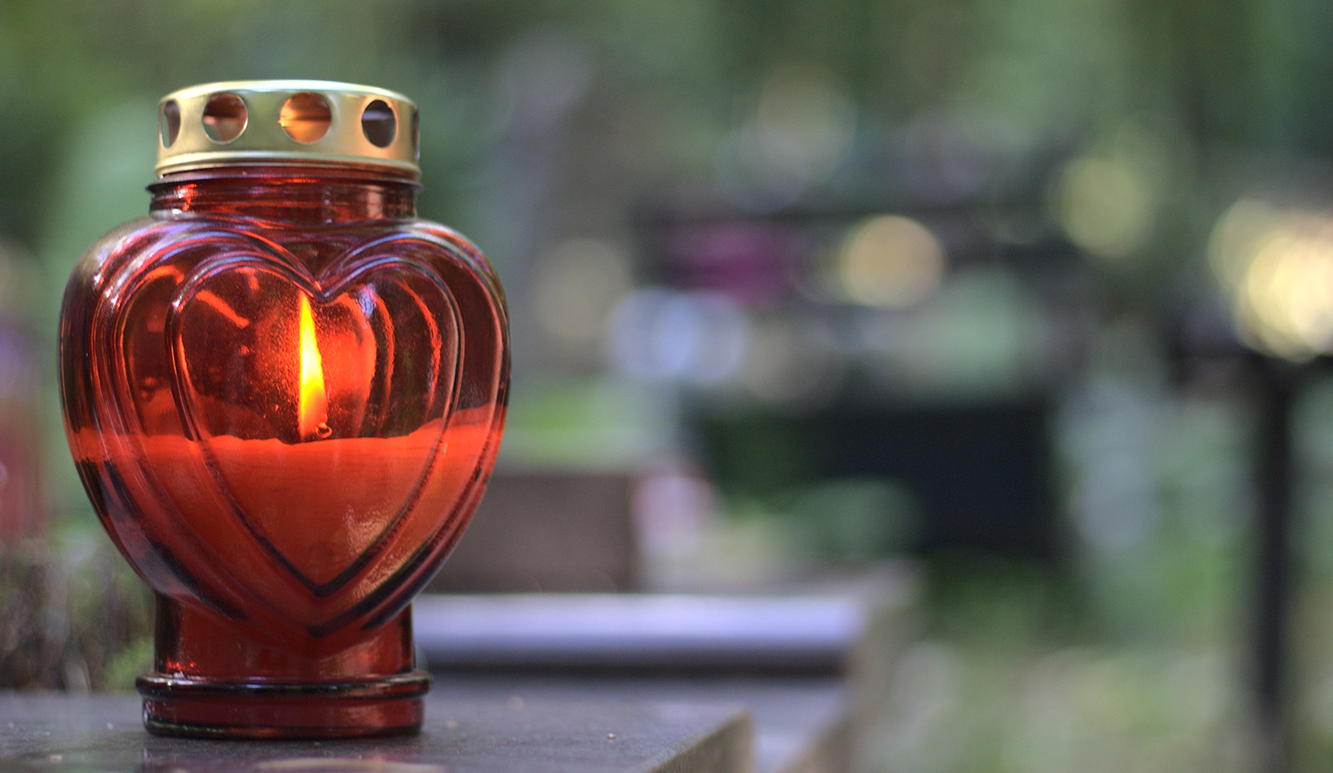 Egy piros, szív alakú gyertya egy sírkövön egy temetőben