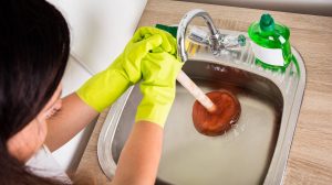 Nő gumikesztyűben pumpálja a lefolyót