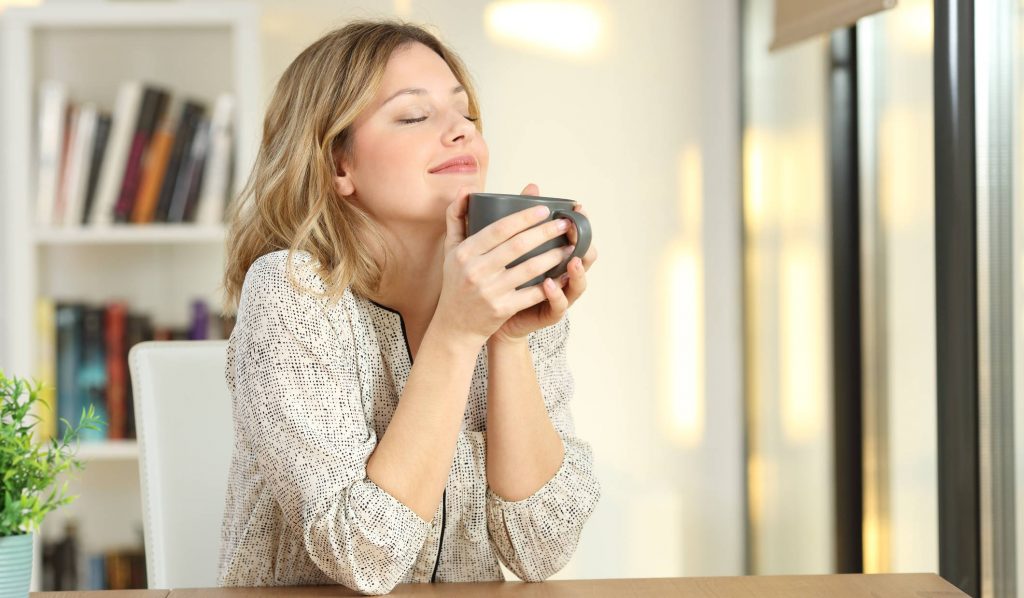 nő az otthonában mély lélegzetet vezs és becsukja a szemét kezében tea vagy kávé