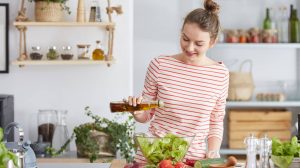 nő a konyhában olívaolajat locsol a salátára