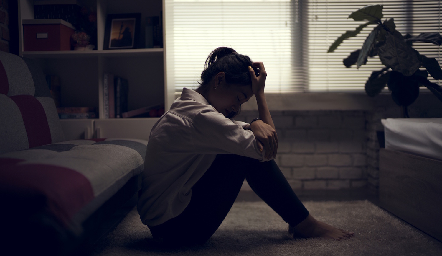 Egy nő elkeseredve ül a sötét szobában