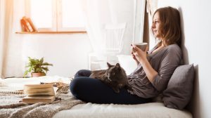 Nő teázik az ágyában és macska van az ölében