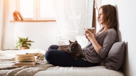 Nő teázik az ágyában és macska van az ölében