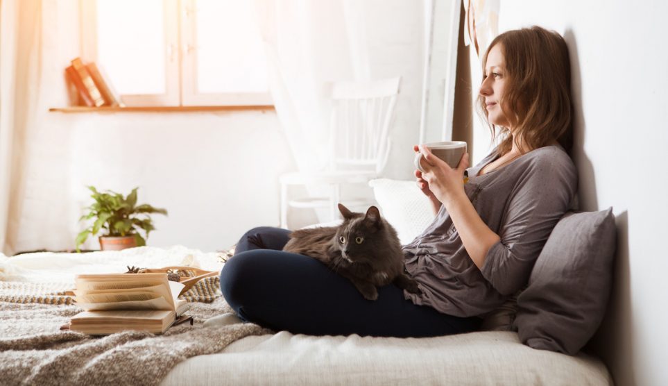 Nő teázik az ágyában és macska van az ölében