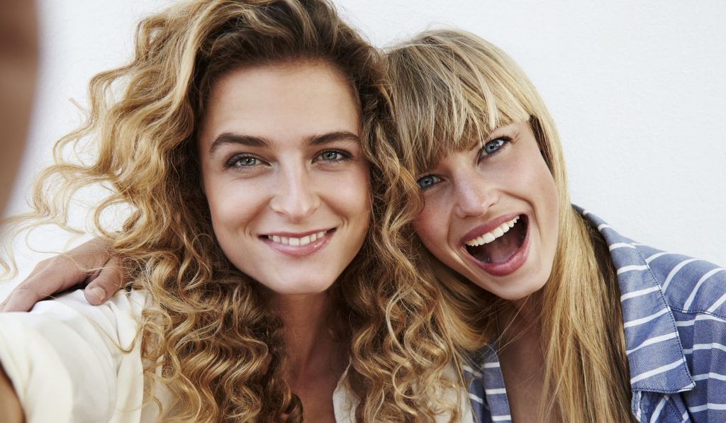 Két fiatal nő ölelkezve mosolyognak