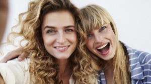 Két fiatal nő ölelkezve mosolyognak