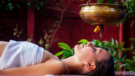 Fiatal nő shirodhara kezelést kap egy faasztalon fekve egy indiai szalonban