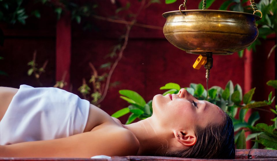 Fiatal nő shirodhara kezelést kap egy faasztalon fekve egy indiai szalonban