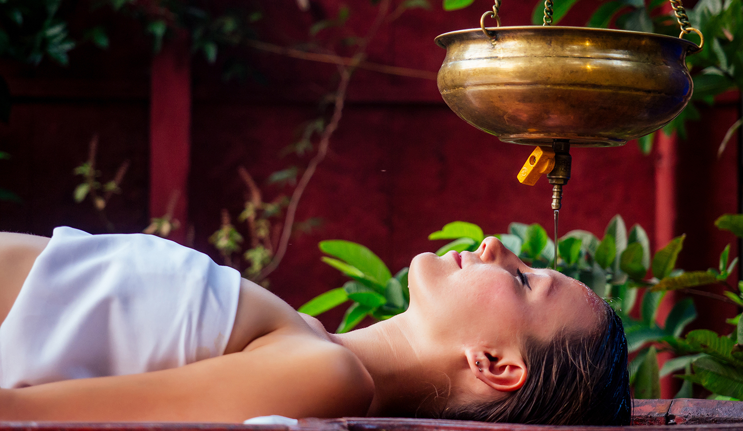 Fiatal nő shirodhara kezelést kap egy faasztalon fekve egy indiai szalonban