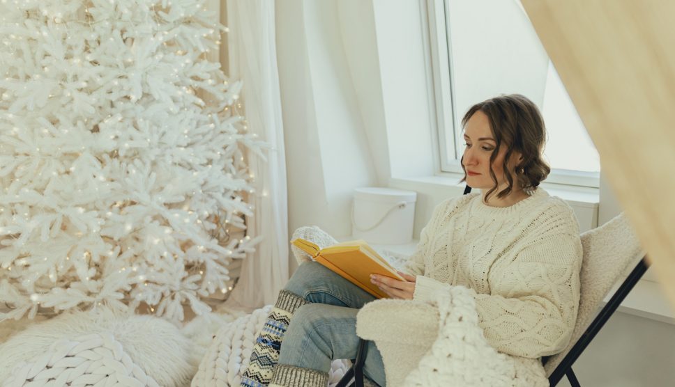 hófehér függönyök előtt ül a karácsonyfánál nő karácsonykor