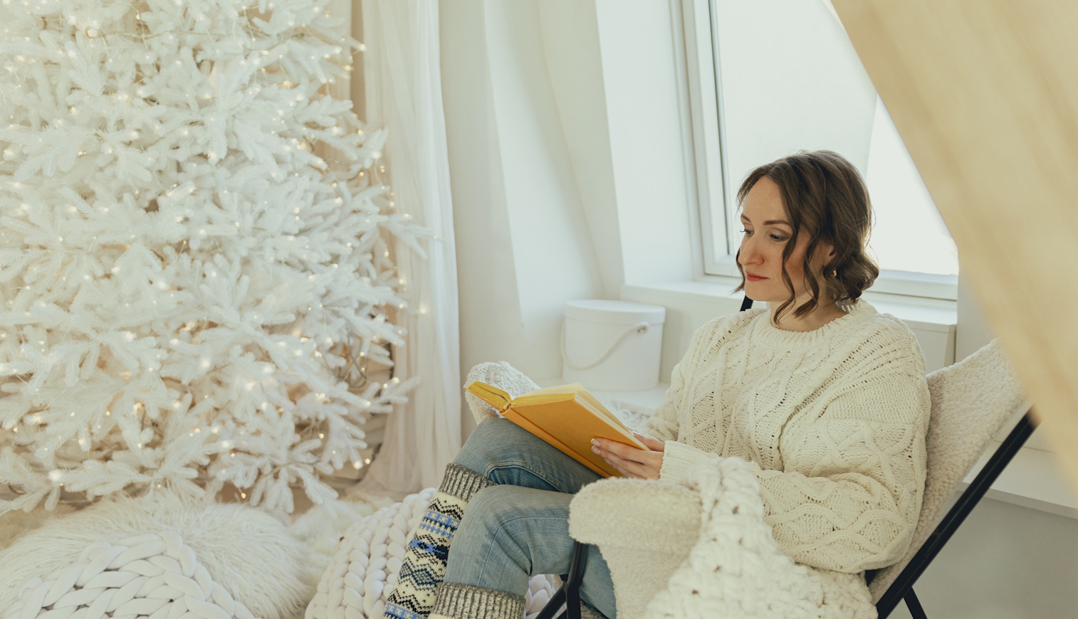 hófehér függönyök előtt ül a karácsonyfánál nő karácsonykor