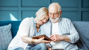 Idős házaspár boldogan nézi az ölükben levő tablettet a kanapén