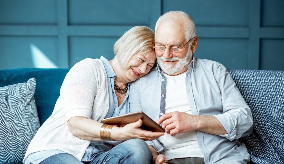 Idős házaspár boldogan nézi az ölükben levő tablettet a kanapén