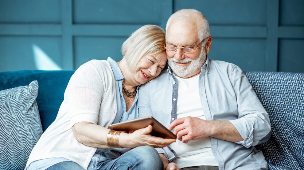 Idős házaspár boldogan nézi az ölükben levő tablettet a kanapén