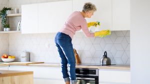 konyhaszekrényt takarít zsírtól egy idős nő