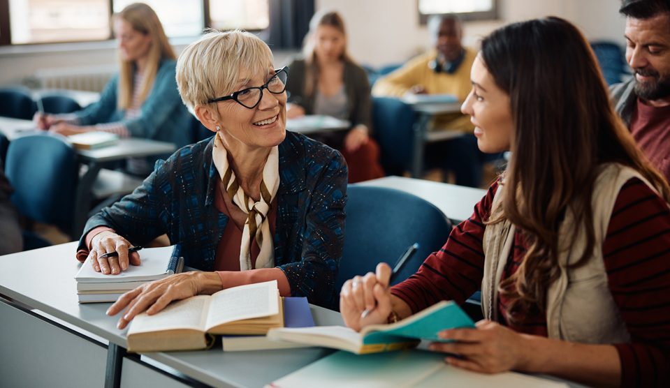 Idősebb nő beszélget fiatalabb osztálytársával az osztályteremben tartott oktatási kurzus során.