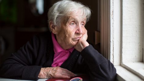 Egy idős nő néz ki az ablakon