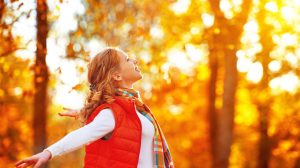 nő szétnyitott karral az őszi falevelek között